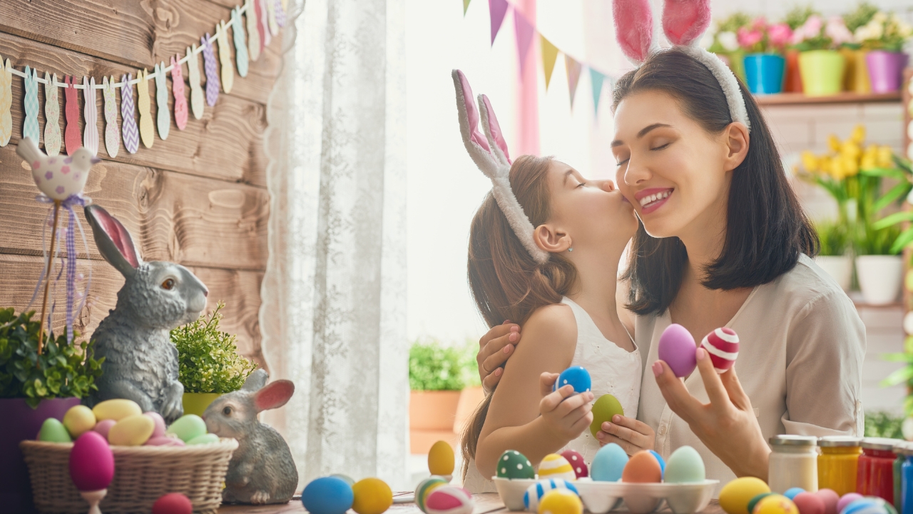Mother and daughter paint Easter eggs at home with bunny ears and colorful decorations