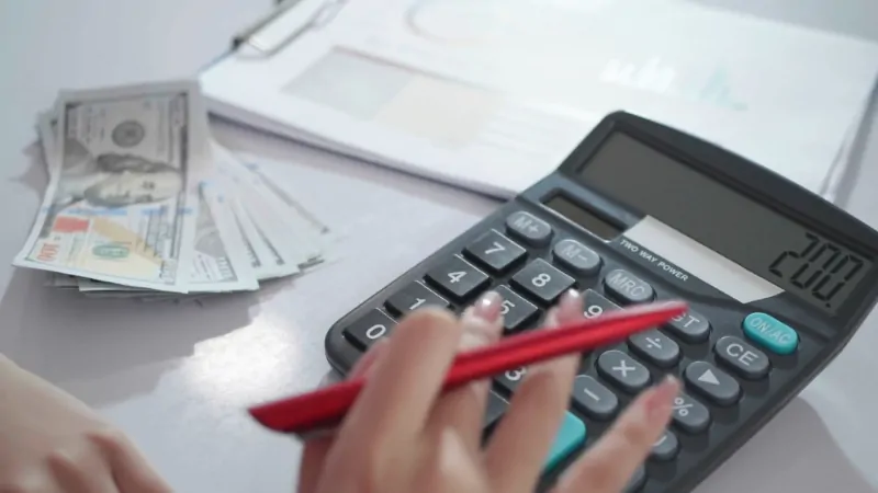 Person using a calculator next to a stack of cash and financial documents related to healthcare costs