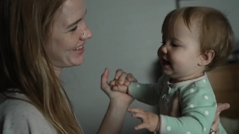 A woman smiles and holds a young toddler in her arms at home, illustrating a caring moment related to adopted children