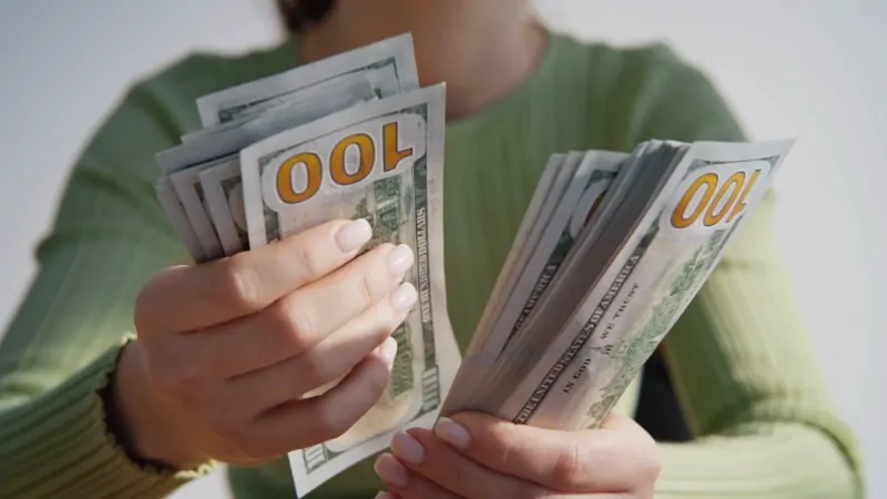 Person holding stacks of hundred-dollar bills, representing teacher pay in the United States