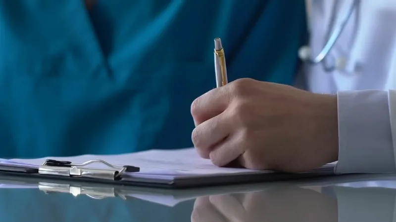 Doctor writing notes on a medical form while reviewing patient information in a clinical setting