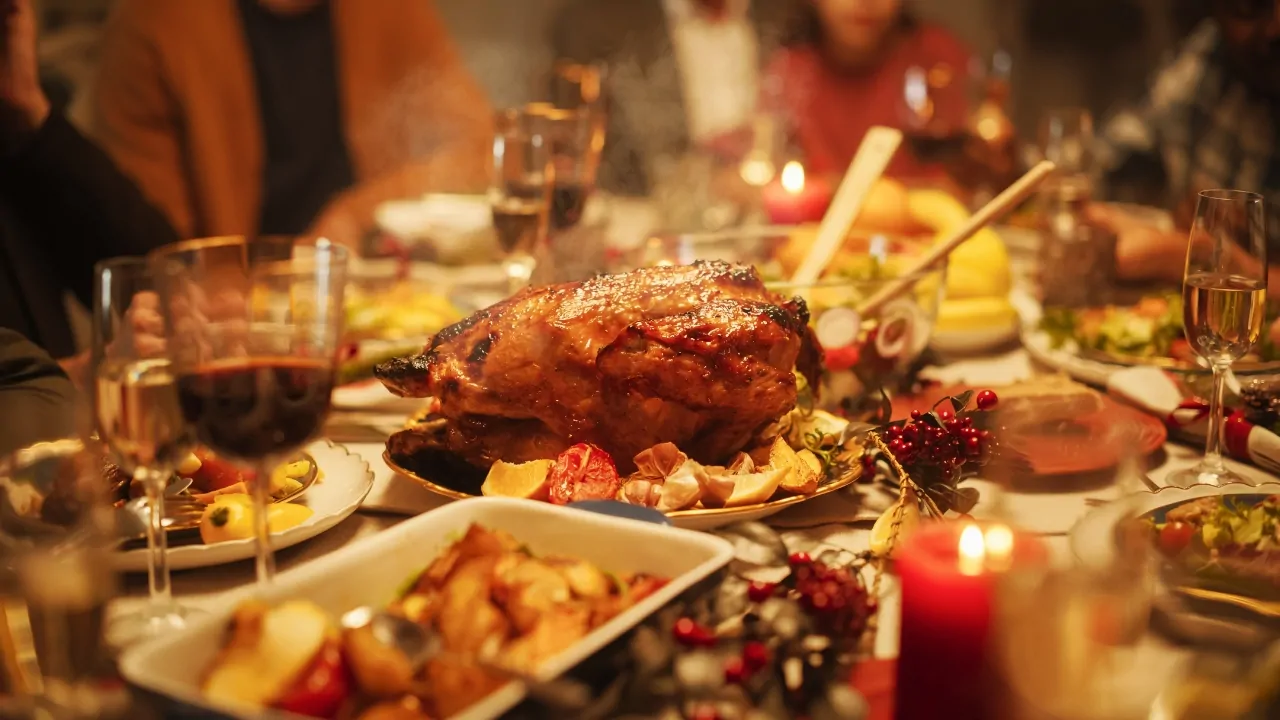 Thanksgiving dinner table with roasted turkey, candles, drinks, and family gathered around