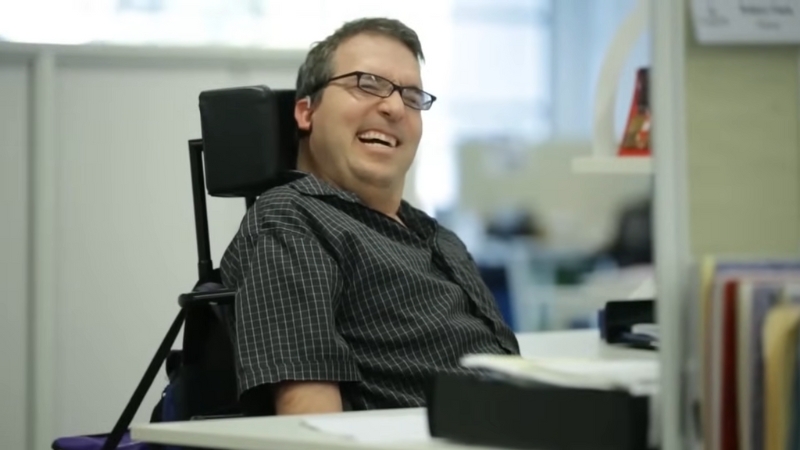 A man with cerebral palsy smiles in an office setting
