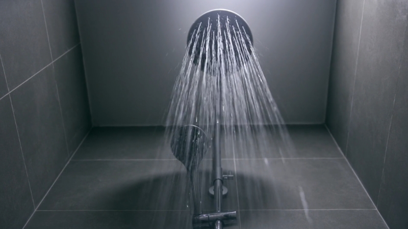 A showerhead releases steady streams of water in a clean, tiled bathroom