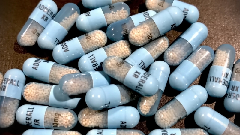 Blue Adderall XR capsules scattered on a surface