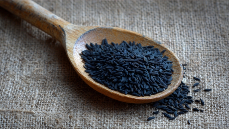 Wooden spoon filled with black cumin seeds on a coarse fabric surface