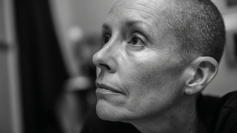 A woman with very short hair looks upward with a calm, thoughtful expression