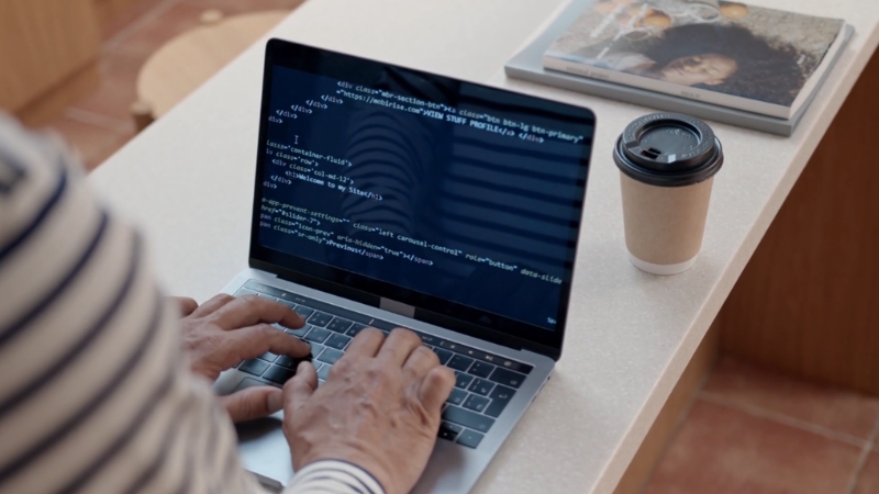 Person coding on a laptop at a desk with a coffee cup beside it
