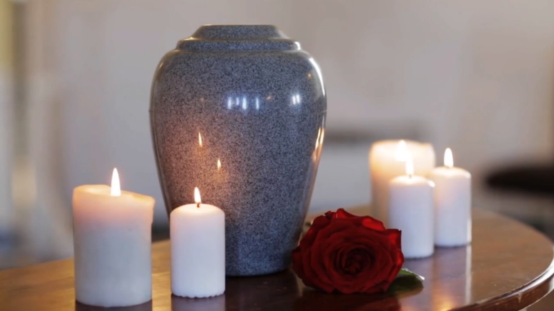 An urn on a table with white candles and a red rose