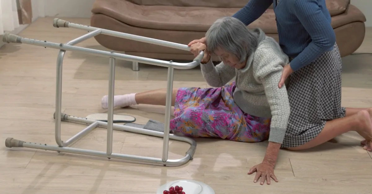 An older woman on the floor after a fall gets support from a caregiver, showing how falls can affect life expectancy