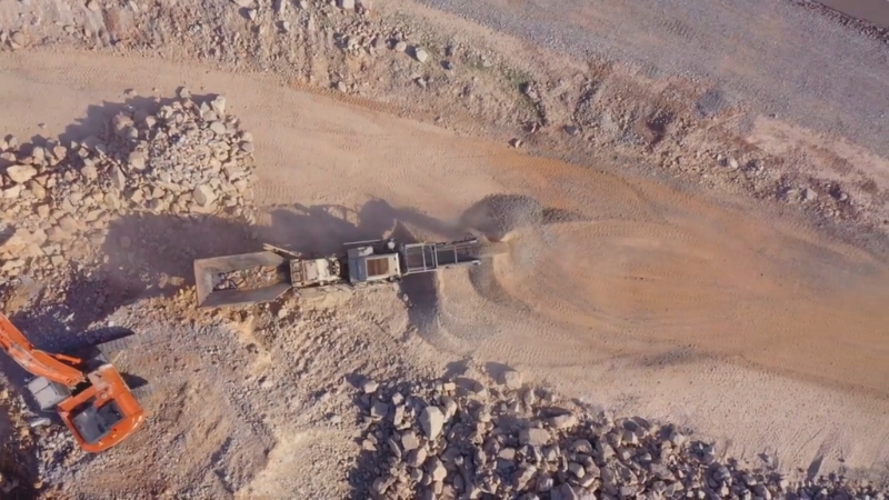 A machine moves gravel and rock at a large open work site