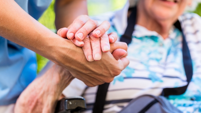 A caregiver gently holds an older adult’s hand during recovery after a fall