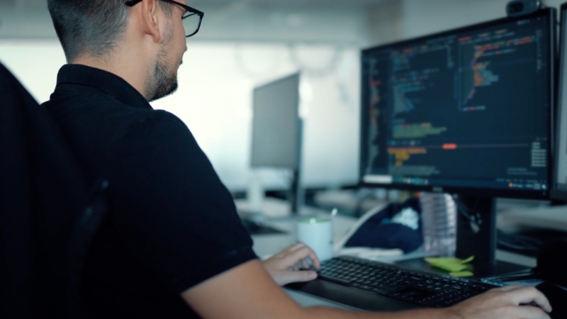 Developer works at a desk with code on a dual monitor setup