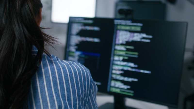 A developer views code on dual monitors in an office setup