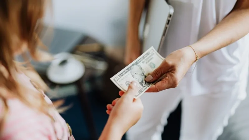 Patient handing cash to a healthcare worker highlighting high out-of-pocket costs in the US compared to Europe