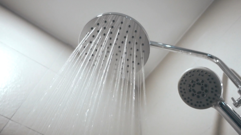 A showerhead releases a steady stream of water in a bright bathroom