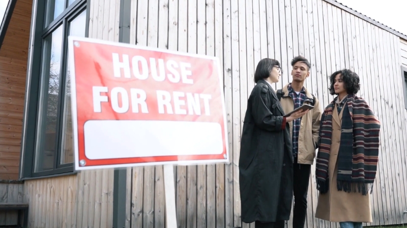 Three renters stand outside a house for rent sign, reflecting limited affordable rental options