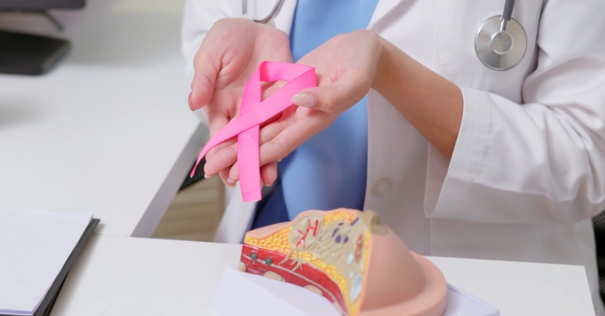 Doctor holds a pink ribbon beside a breast model to explain breast cancer risk linked to alcohol