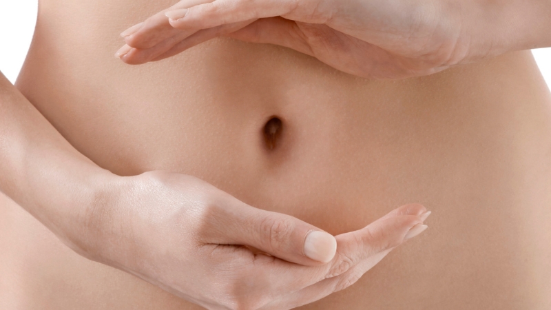 Close-up of a person’s abdomen with hands near the belly button highlighting the navel area