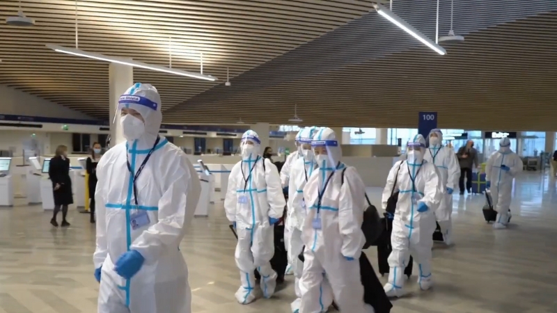 Airport staff in full protective suits walk through a terminal during heightened health screening measures