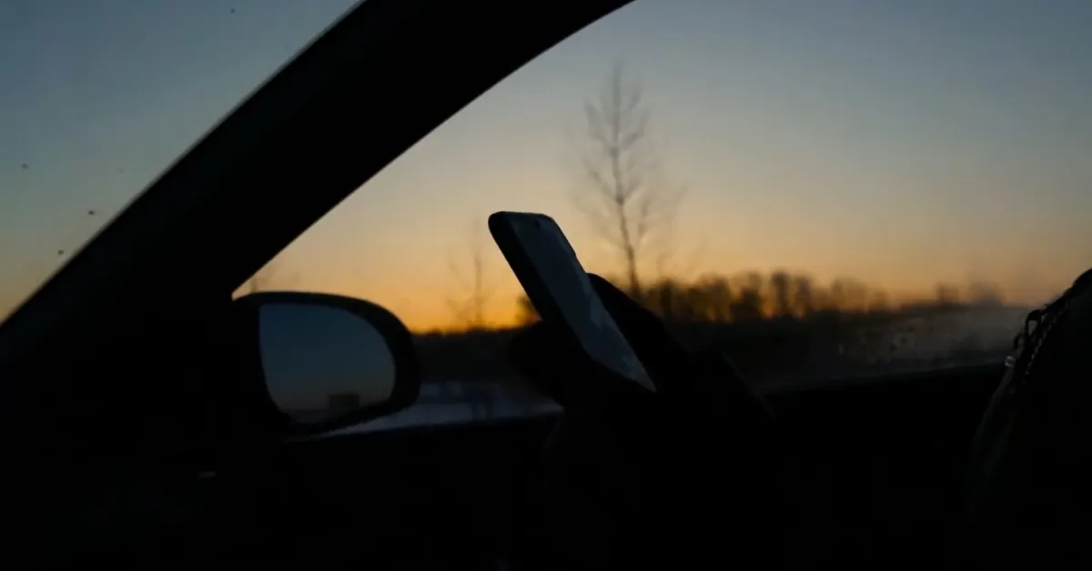 Driver looking at a phone inside a car at sunset, showing distracted driving in Colorado