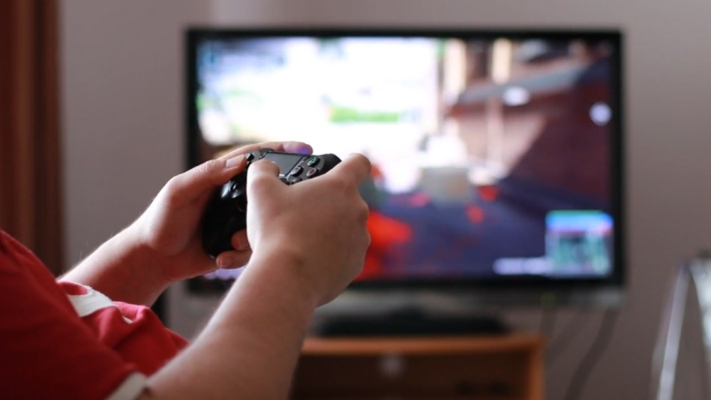 A person holds a game controller while playing a video game on a TV screen at home