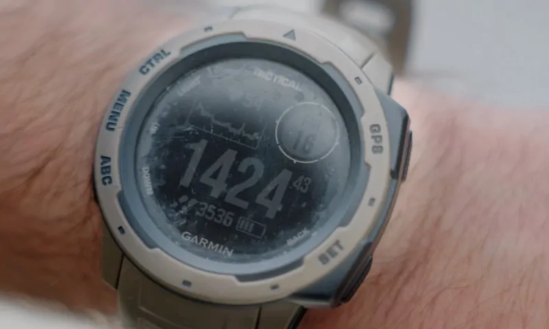 A rugged digital watch with a scratched face on a wrist, showing large numbers, graphs, and the brand โGarmin.โ
