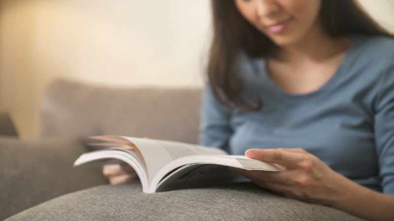 Woman sits on a couch and reads a book at home