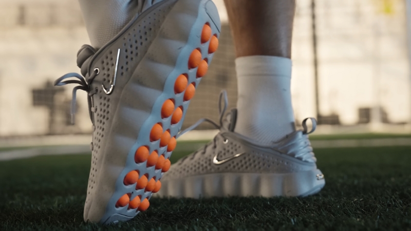 Person wearing Nike shoes with textured orange pods on the sole while standing on grass