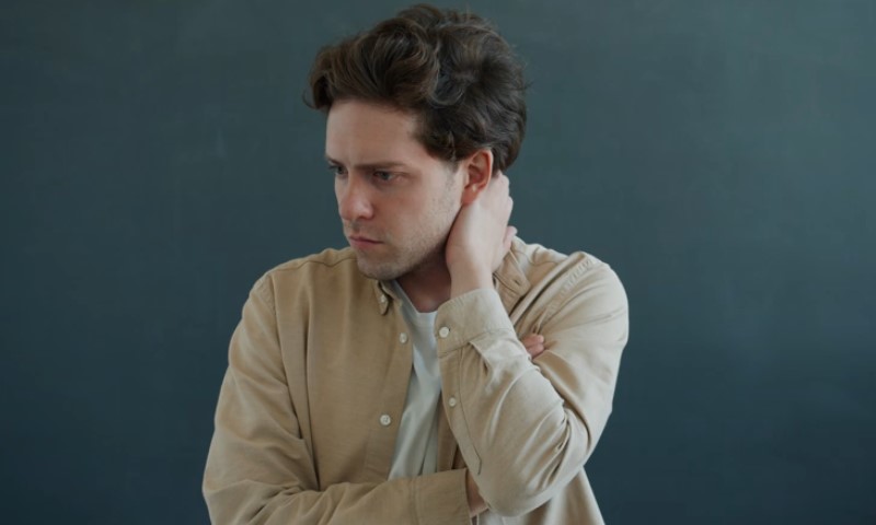 A man with curly hair looks worried, holding his neck with his right hand