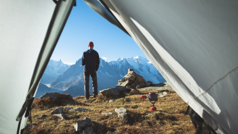 Camper stands outside a tent looking over a mountain landscape with camping gear nearby