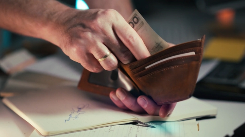 A hand pulls cash from a wallet beside paperwork