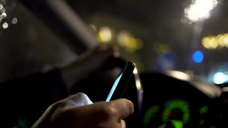 Driver holding a phone behind the wheel at night, illustrating distracted driving in Colorado