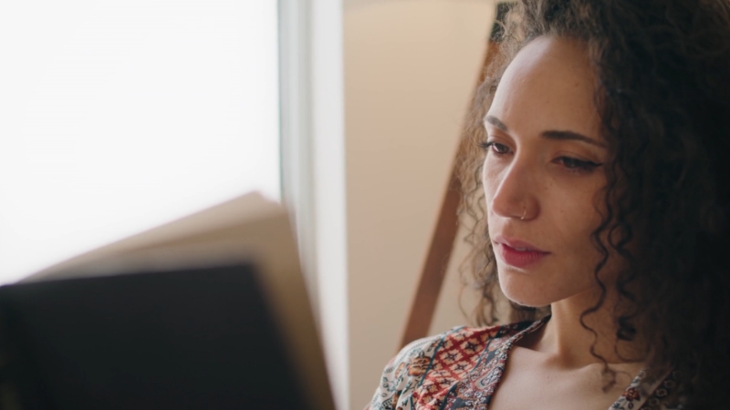 Woman reads a book near a window with focused attention