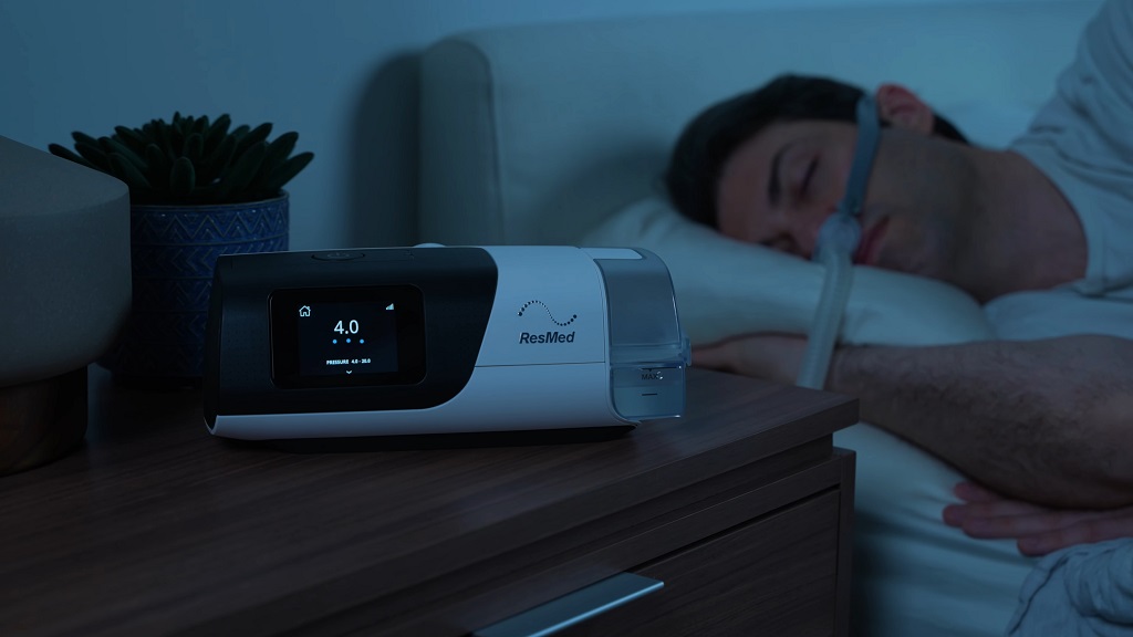 Man sleeping in bed while using a CPAP machine placed on a bedside table