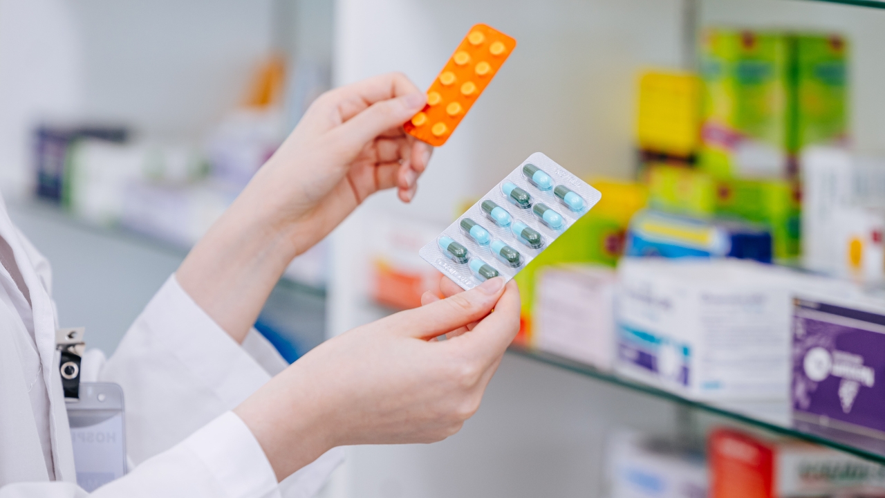 Pharmacist holding two blister packs of common medicines in a pharmacy