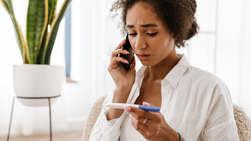 Woman holding a pregnancy test and speaking on the phone, illustrating reproductive health concerns