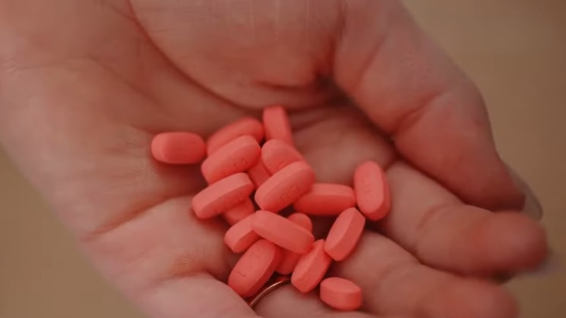 Hand holding several pink azithromycin tablets used to treat bacterial infections