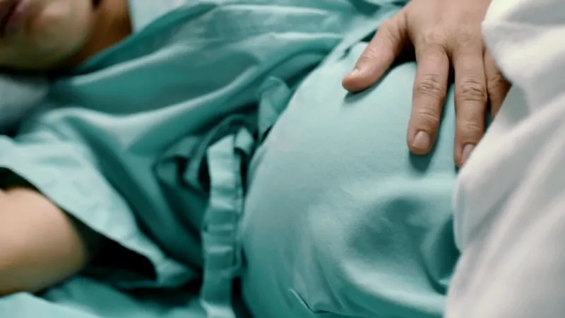 Close-up of a pregnant woman lying in a hospital bed with a hand resting on her belly
