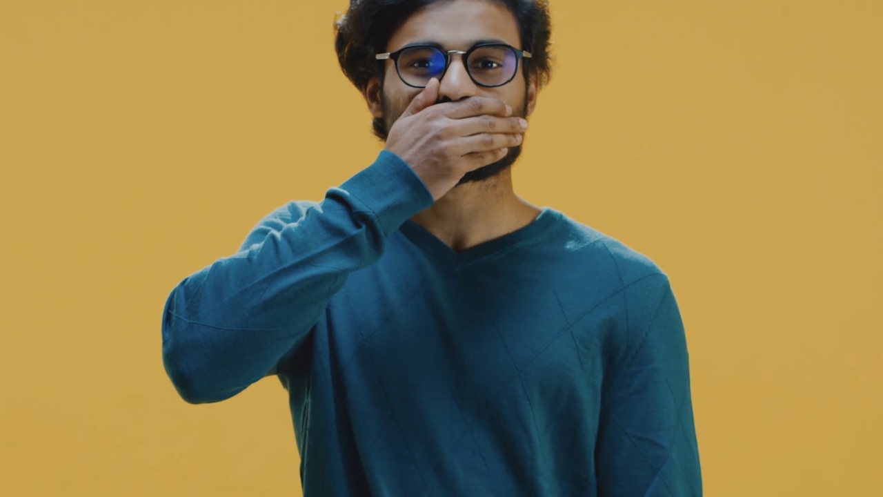 Man covering his mouth as if trying to stop hiccups against a plain yellow background