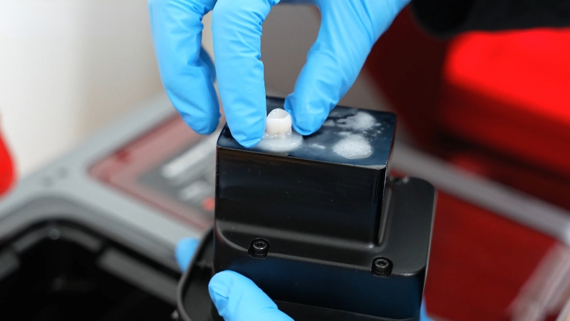 Dental technician placing a freshly printed ceramic crown on a chairside 3D printer platform during in-clinic fabrication