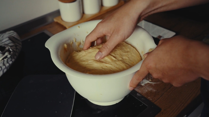 Hands kneading bread dough in a large mixing bowl on a kitchen counter