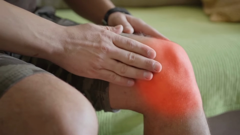 Person holding a swollen knee highlighted in red to show pain or inflammation after injection