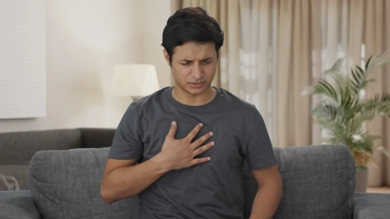 Man sitting on a couch holding his chest as he experiences long Covid symptoms