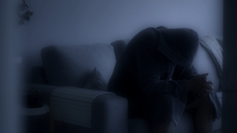 Silhouetted person sits hunched on a couch with head in hands, conveying emotional distress