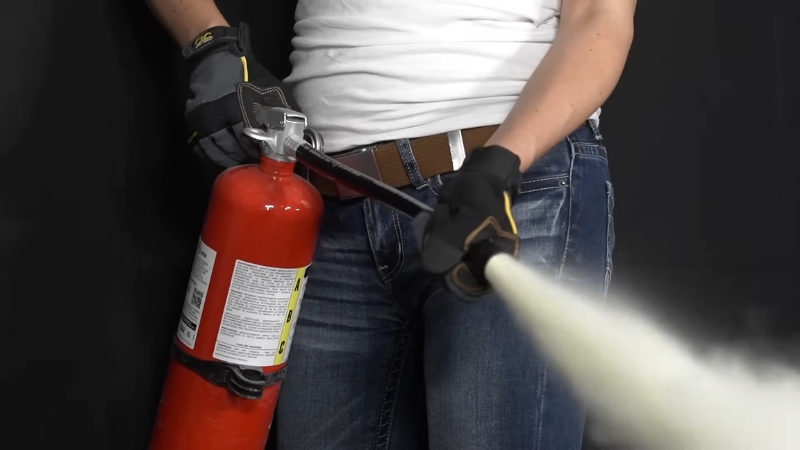 A worker wearing gloves uses a fire extinguisher to spray a safety demonstration