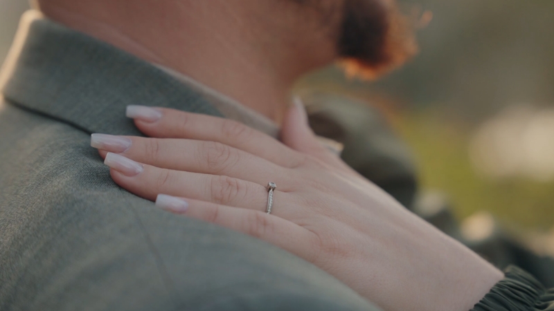 Close-up of a woman’s hand with an engagement ring resting on a man’s shoulder outdoors