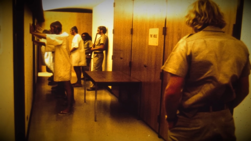Participants in prison uniforms stand in a hallway during the Stanford Prison Experiment simulation
