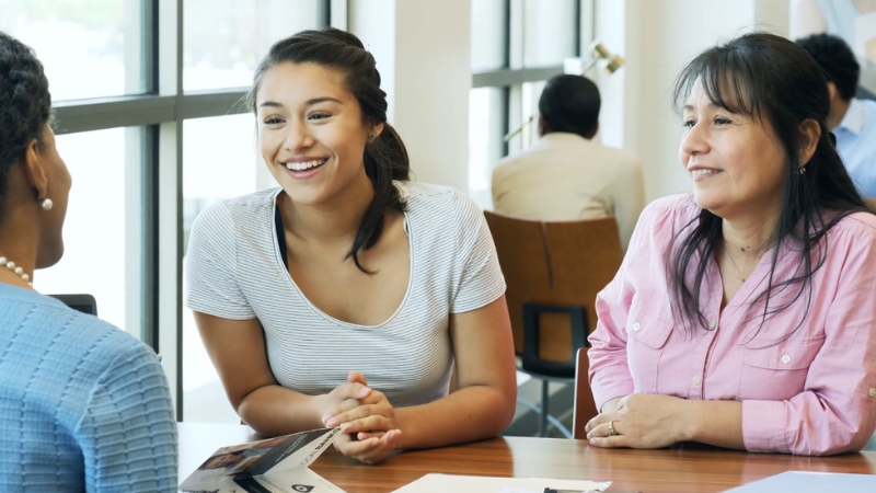 Two women speaking with a financial advisor at a desk about student loan repayment options