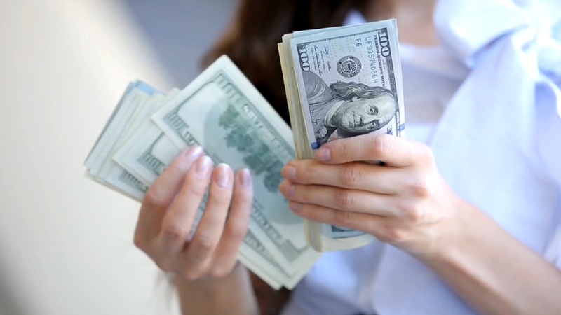 Person holding a stack of U.S. dollar bills, symbolizing student loan debt relief and policy debates